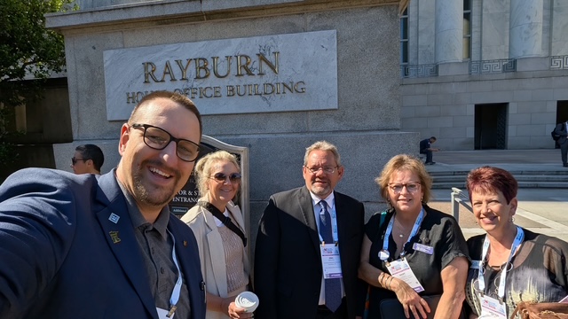 Five Realtors in front of the Rayburn Office Building in DC with the sun shining in their face while they smile. All are dressed in professional attire.